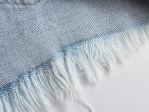 Detail of light blue denim shorts with distressed raw hem and frayed fringe edges