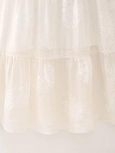 Close-up of elegant white floral embroidery on halter neck dress with pleated ruffle hem