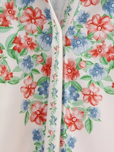 Gros plan sur l'imprimé floral rouge et bleu sur un chemisier blanc cassé à col en V