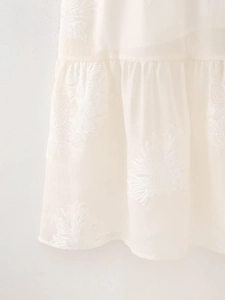 Detail of white summer dress featuring floral embroidery and ruffled hemline texture