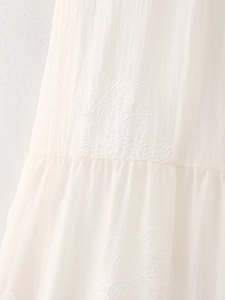 Macro detail of white dress featuring textured ripple fabric and floral embroidery