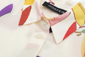 Close-up of collared shirt neckline featuring colorful abstract print and resin buttons