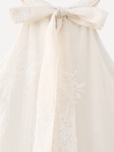 Detail of elegant cream white dress featuring intricate floral embroidery and a large bow tie