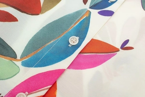 Detailed close-up of vibrant leaf print and white button on summer poplin shirt