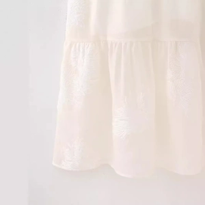 White jacquard halter dress with intricate feather embroidery and pleated hem detail