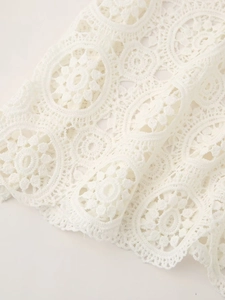 Close-up detail of white floral crochet lace fabric with intricate hollow embroidery