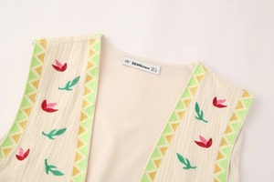 Close-up of floral embroidery and geometric stitching on cream cotton vest neckline