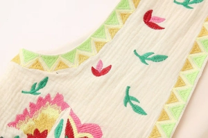 Detail of vintage sleeveless vest featuring colorful floral embroidery and pleated texture