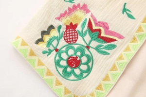 Macro shot of colorful floral embroidery and geometric patterns on a beige linen vest