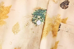 Detailed close-up of a leaf print shirt featuring white buttons and a chest pocket