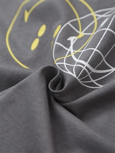 Detail of yellow fluid smiley face and white mesh pattern printed on dark grey cotton T-shirt
