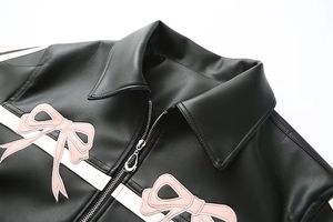 Détail d'une veste en similicuir noir avec broderie nœud rose et rayures blanches
