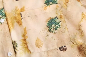 Detail of chest pocket and white buttons on a beige forest print shirt