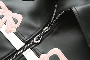 Détail macro de la veste en cuir PU noir avec zip argenté et broderie nœud rose