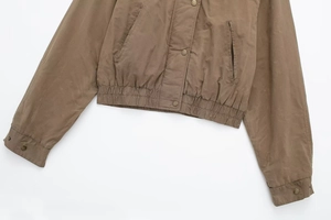 Detail of tan bomber jacket showing metal snap buttons and elastic ribbed hemline