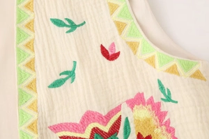 Detail of colorful floral embroidery and textured cream fabric on a retro sleeveless vest