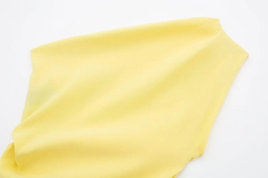 Detaillierte Makro-Textur des hellgelben Plissee-Stoffes auf dem asymmetrischen Sommertop