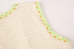 Detail of cream vest with vertical texture and colorful geometric embroidery on the neckline