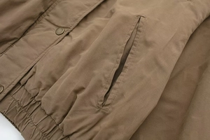Detail of tan bomber jacket showing slanted pocket and elastic hem with metal hardware