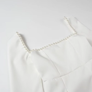 Detail of square neckline with elegant white pearl trim on a woven dress fabric