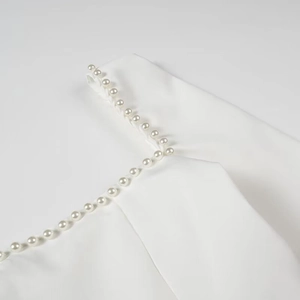 Detail shot of elegant white dress neckline featuring handcrafted pearl embellishments