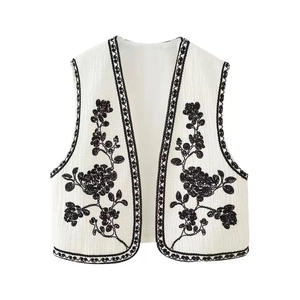 Detail of vintage beige vest with black floral embroidery and wavy textured lace trim