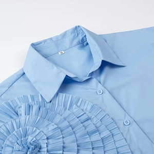 Detail of light blue shirt featuring a large pleated 3D floral appliqué and pointed collar