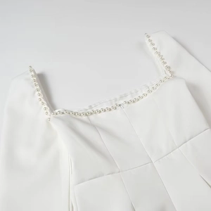 Close-up of a white square-neck dress featuring elegant pearl trim and a hidden zipper
