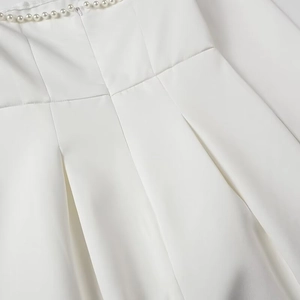 Detail of white dress featuring elegant pearl embellishments and pleated fabric texture