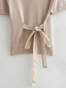Close-up of beige knitted top featuring elegant silk bow tie details on the back