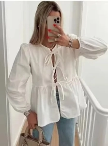 Close-up of white long sleeve blouse with three front bow ties and ruffled hem details