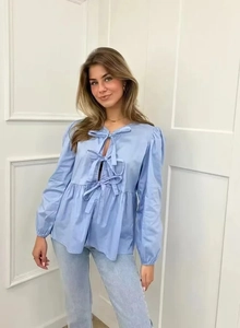 Detail of light blue shirt featuring bow-tie front closures and peplum hem design