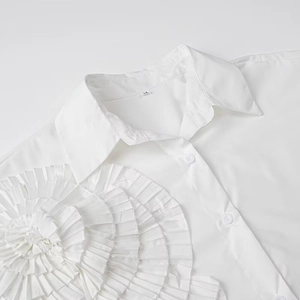 Detailed view of large 3D pleated floral appliqué on a white long-sleeve cotton shirt