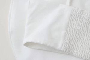 Detail of white cotton poplin fabric featuring smocked elastic texture and fine stitching