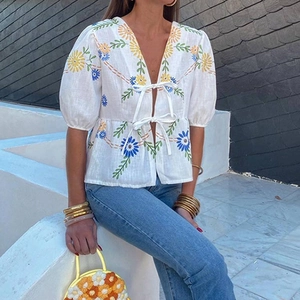 Detail of bohemian white linen blouse featuring floral embroidery and ribbon front ties