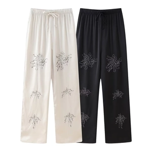 Detail of beaded floral patterns on elastic drawstring pants in cream and black