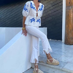 Detail of white linen top featuring blue floral embroidery and stylish front tie closures