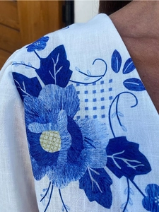 Detailed close-up of blue floral embroidery on a white linen shirt for women