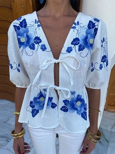 Detail of white linen top featuring blue floral embroidery and front bow tie closures