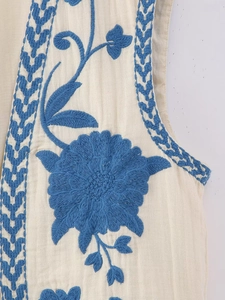 Detailed view of bohemian floral embroidery and blue woven trim on cotton linen vest