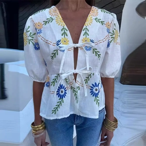Close-up of white linen shirt featuring colorful daisy embroidery and bow-tie closure