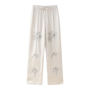 Detail of high-waist cream trousers with floral print and elastic drawstring waistband