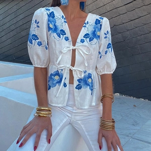 Detail of floral embroidery on a white linen blouse with front ties and puff sleeves