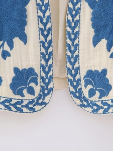 Detail of vintage floral embroidery on the hem of a cream white bohemian style vest
