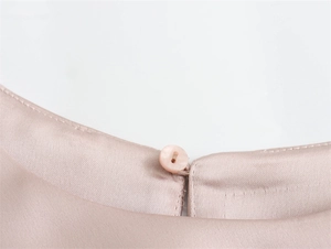 Détail de l'encolure en satin champagne montrant la texture fluide et la fermeture à bouton