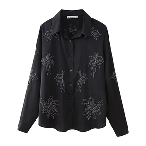 Detail of black long-sleeved silk-like shirt with white beaded floral embroidery and buttons