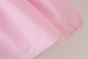 Detail of pink blouse showing fine fabric texture, stitched hem, and elastic ruffled edges