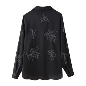Detail of beaded radial floral patterns on the back of a black satin shirt