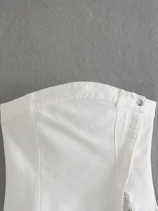 Dettaglio del top a fascia in denim bianco con cuciture, bottone metallico e bordi sfrangiati