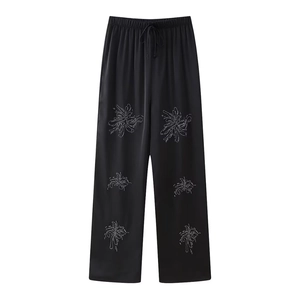Detail of black wide-leg pants with elastic waist and sparkling floral rhinestone embroidery